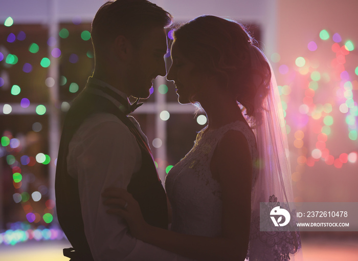 Cute happy wedding couple dancing against defocused lights