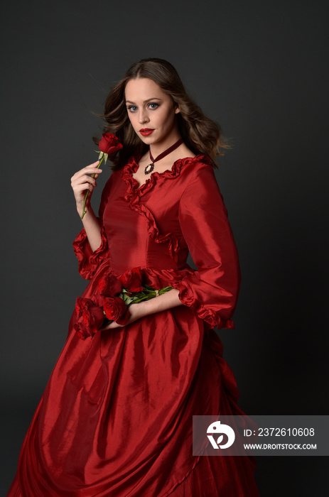 portrait of pretty female model with red hair wearing glamorous historical victorian red ballgown.  