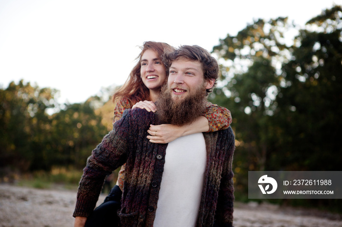 Bearded man giving his girlfriend piggyback ride outdoors