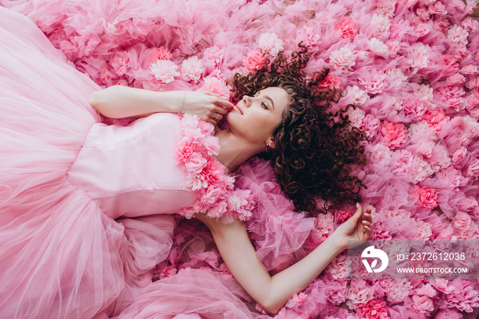 一个穿着粉色连衣裙的漂亮女孩的近照。一个卷发的年轻女人躺在粉色的花朵上