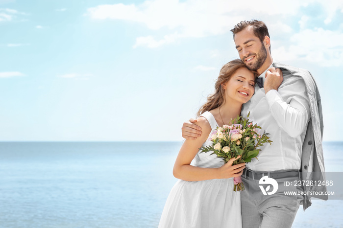 Happy newlywed couple hugging on seashore