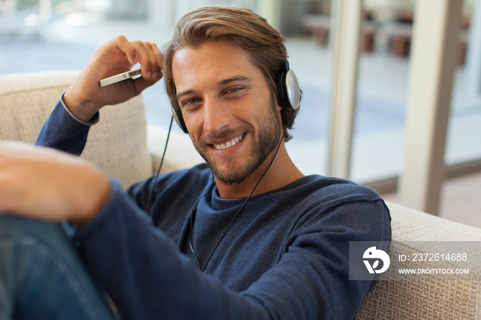 Portrait smiling young man listening to music with headphones on sofa