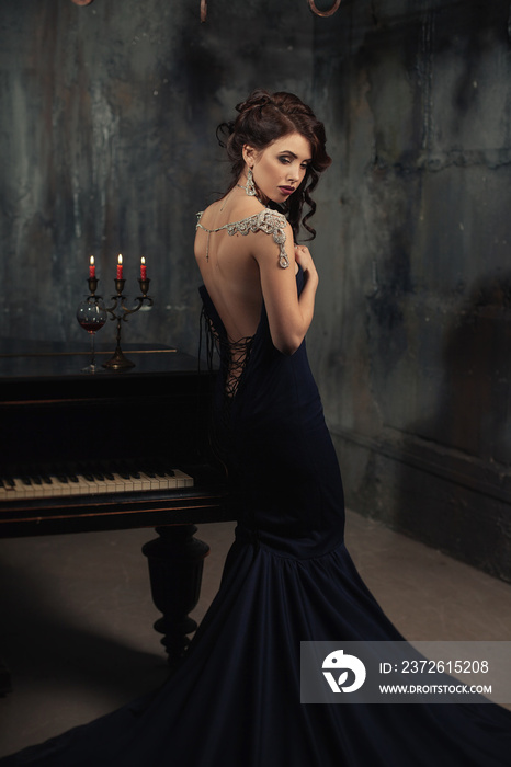 美丽的年轻女子穿着黑色连衣裙，坐在钢琴旁，手里拿着烛台、蜡烛和葡萄酒，充满戏剧性