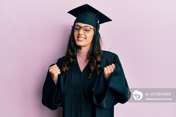 一位身穿毕业帽和典礼礼服的年轻西班牙女性举起双臂，为成功而兴奋