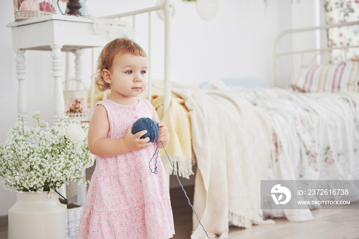 Childhood concept. Baby girl in cute dress play with colored thread. White vintage childroom