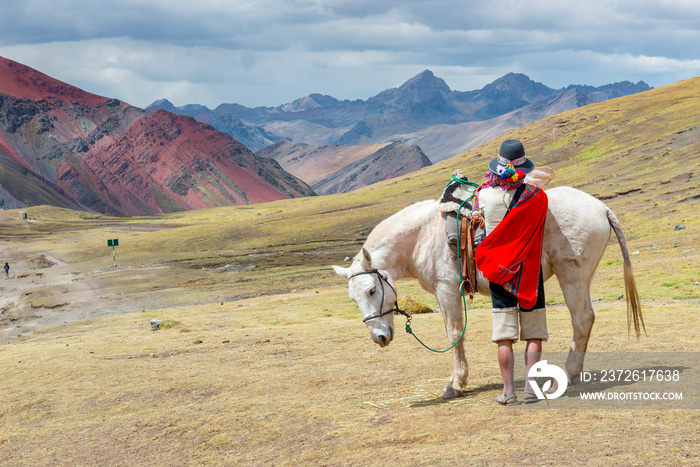 Man dressed in traditional clothing with a horse in Rainbow Mountain, near Cusco, Peru