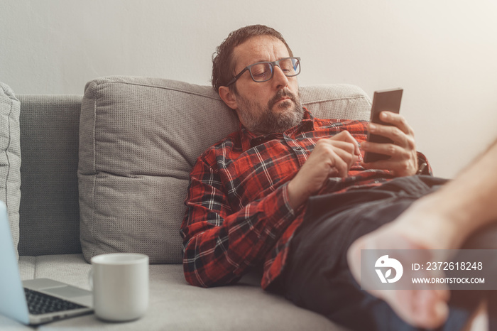 Laid back barefoot casual man taking a break on mobile smart phone while working from home