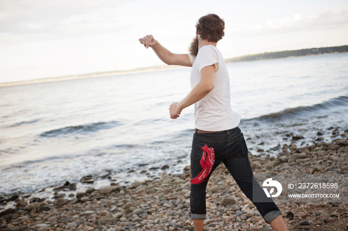 Young man on beach throwing pebbles into sea