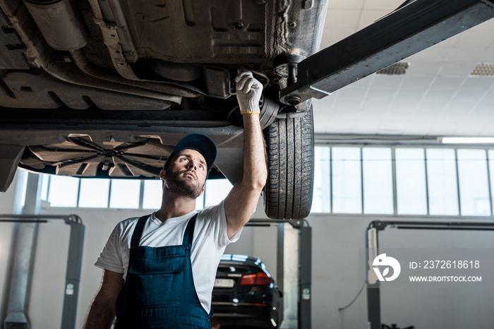 bearded car mechanic in cap looking at automobile in car service