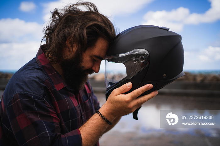 Bearded man putting his front next to his motorbike helmet