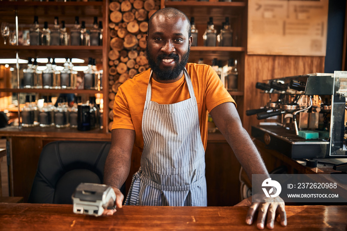 Cheerful male barman holding terminal for contactless payment