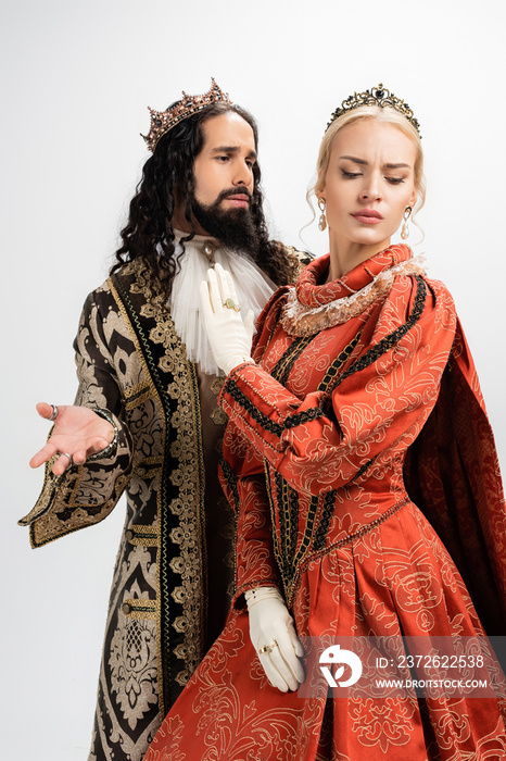 hispanic king in crown and medieval clothing looking at displeased blonde wife isolated on white