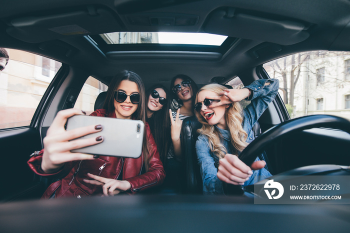 Group of girls having fun in the car and taking selfies with camera on road trip