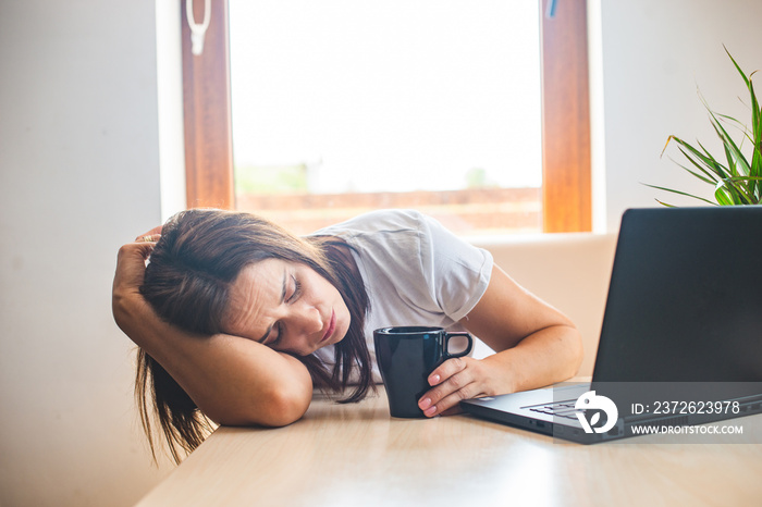 Tired businesswoman sleeping on table in office. Young exhausted girl working from home. Woman using