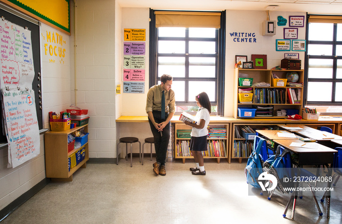 Student reading book in front of teacher in classroom