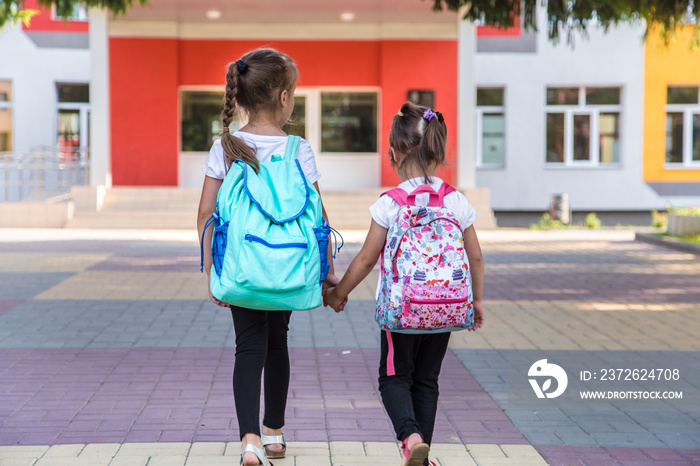 Back to school education concept with girl kids, elementary students, carrying backpacks going to cl