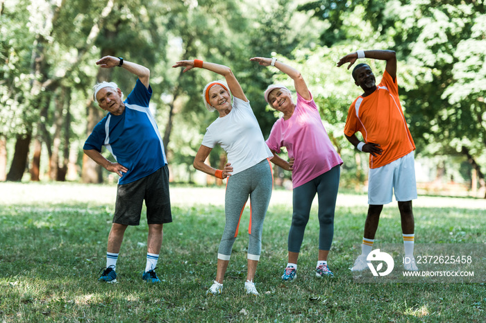 cheerful multicultural retired men and women standing with hands on hips while doing stretching exer