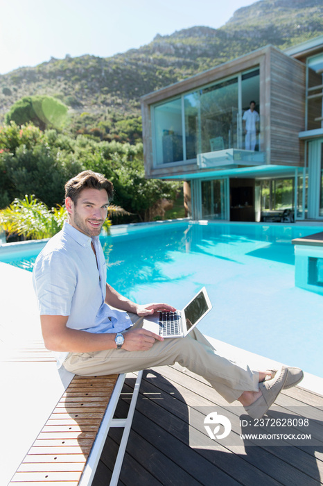 Portrait young man using laptop at sunny luxury poolside