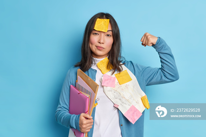 Powerful female student raises arm and shows muscles feels confident after working on diploma paper 