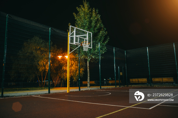 照亮的篮球场，红色路面，现代化的新型篮球网和ba上的透镜照明弹