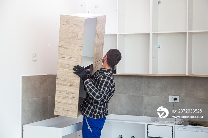 The carpenter places the newly assembled kitchen shelves in the intended place.