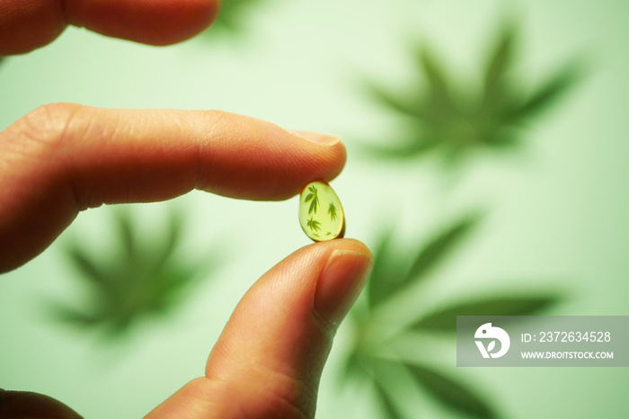 Close up hand holding CBD oil pill. Cannabis leaves reflection. Medical marijuana usage