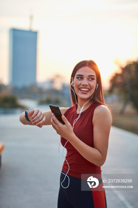 Modern young woman with cellphone making pause during jogging / exercise.