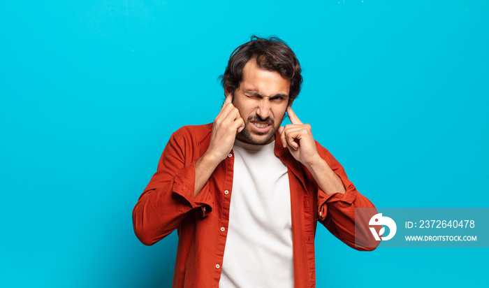 young handsome indian man looking angry, stressed and annoyed, covering both ears to a deafening noi