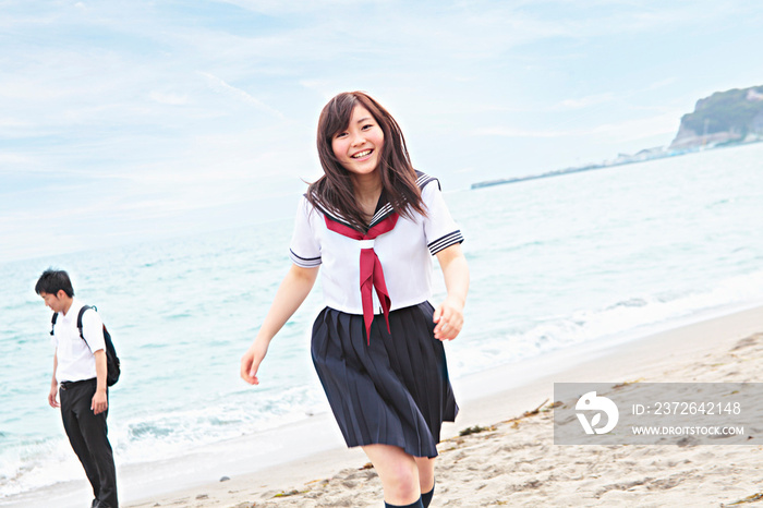 Young woman running across beach wearing school uniform