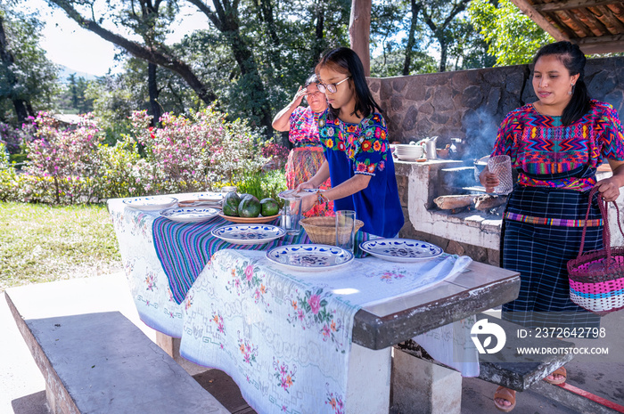 Abuela, Madre e Hija arreglan la mesa para comer. Familia Latina disfrutan el momento al aire libre.