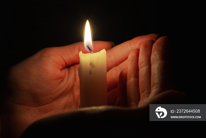 Burning candle in womans hands in dark