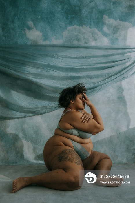 portrait of a plus size afro indigenous person sitting on floor with hand on face