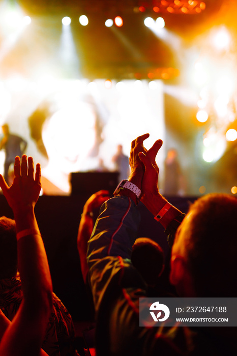 Сrowd with raised hands at music festival. Fans enjoying rock concert with light show and clapping h