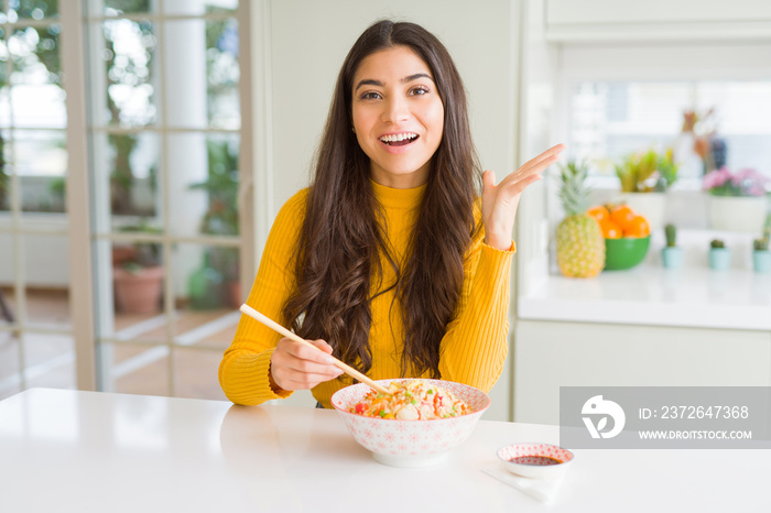 Young woman eating a bowl of Asian rice using chopsticks very happy and excited, winner expression c