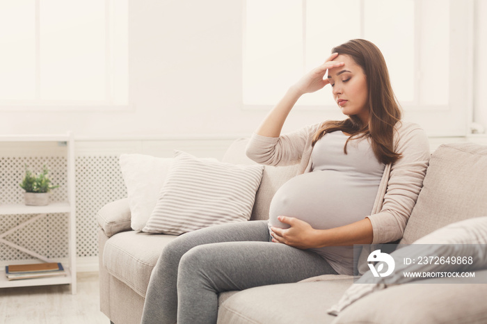 Young pregnant woman with headache sitting on sofa