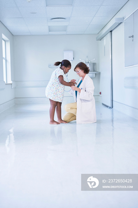 Female doctor using stethoscope on girl patient in hospital childrens ward