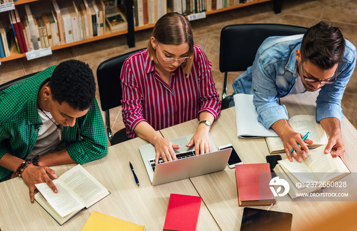 Three young students study in the school library and using laptop for researching online.