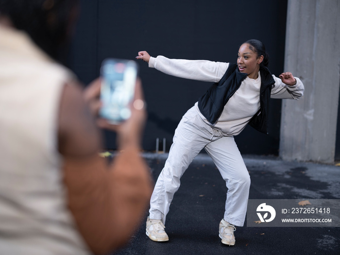 Young woman photographing?friend dancing in city