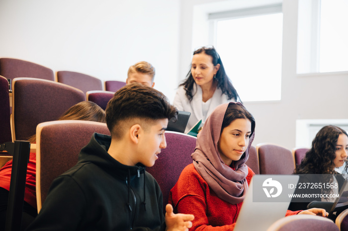 Multi-ethnic classmates using laptop in lecture hall at university