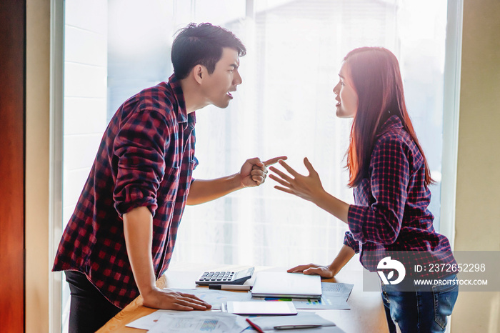 asian coworkers in a disagreement and looking at each other with an angry face, standing up facing o