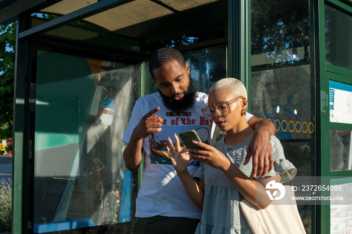 Couple waiting at bus stop and using smart phone