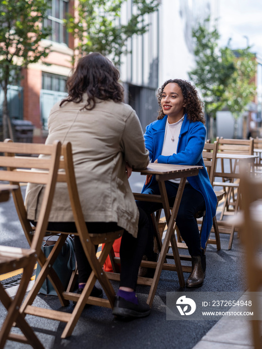 英国，微笑的女同性恋情侣坐在人行道咖啡桌旁