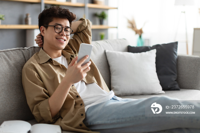 戴眼镜微笑的亚洲男子在家使用智能手机