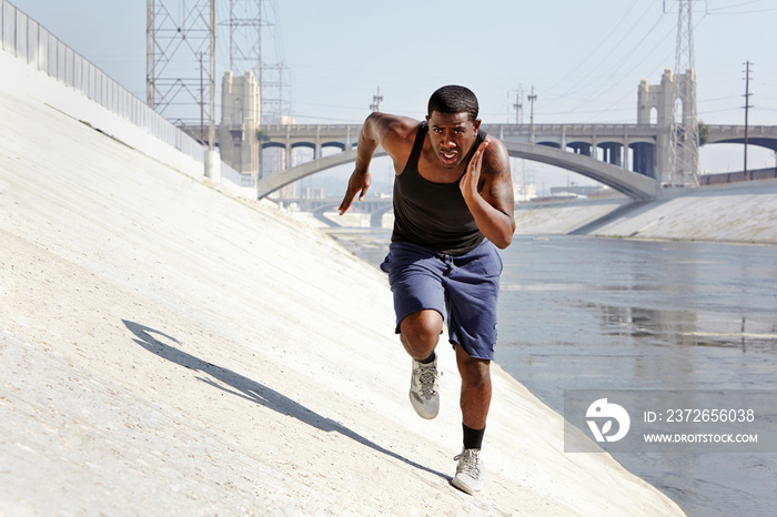 Young man speed running along riverbank