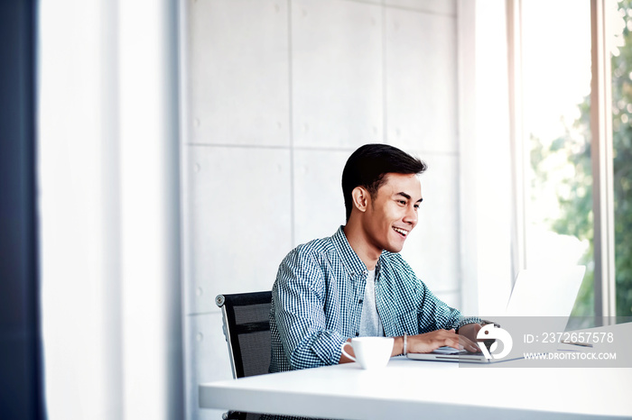 Happy Young Businessman Working on Computer Laptop in Office. Sitting on Desk, Man in Casual Wear