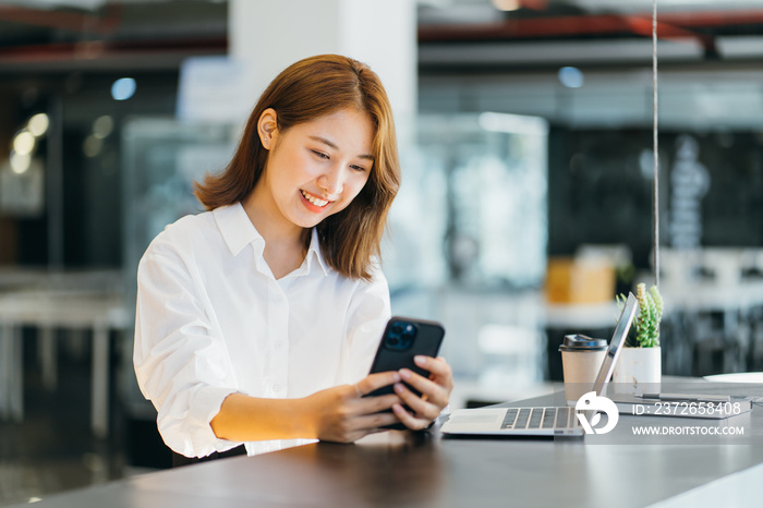 Asian young lady working in the cafe with laptop, holding phone smiling.