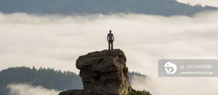 Silhouette of athletic climber tourist on high rocky formation on mountain valley filled with white 