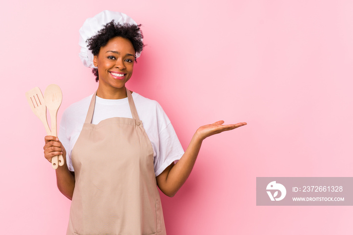 Young african american cook woman showing a copy space on a palm and holding another hand on waist.