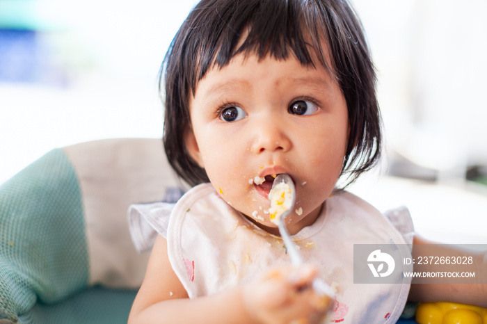 可爱的亚洲女婴自己吃健康食品，脸和手都弄得一团糟