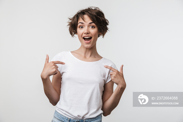 Portrait of positive woman with short brown hair in basic t-shirt rejoicing and pointing fingers at 